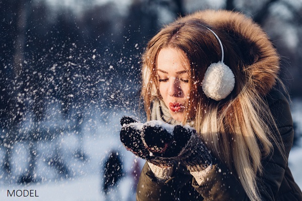 Woman wearing ear muffs blowing snow out of her hands